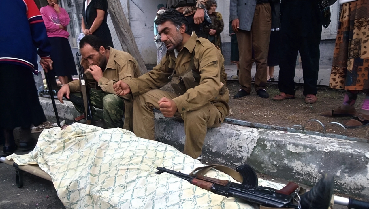 Abkhazian fighters sit on the curb next to a shrouded body. Sukhum. September 1993.